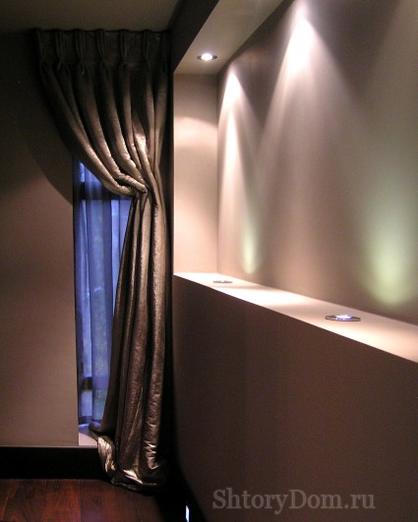 Портьеры на узком окне в коридоре подсвечена встроенными светильниками - вариант асимметричных штор